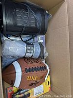 Box containing various new and possibly used items including Wilson football, heater, electric door alarm, flying ring, wallets, and other household and personal items.