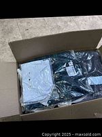 Photo showing a white collared shirt and darker clothing items packed in the box, some items still in plastic bags.