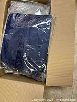 Box containing a navy blue folded garment sealed in plastic.