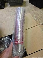 Stack of clear plastic cups with red Budweiser branding, shrink wrapped in sleeves inside an opened cardboard box.