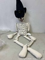 Full view of Ms Bones skeleton pillow seated against wall showing bone details and witch hat