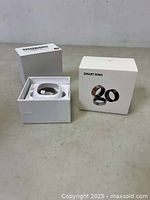 Smart ring in box with protective plastic inside opened showing ring and packaging with original box beside it.