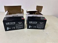 Two UB1270 sealed lead-acid batteries in partially open boxes side by side on white background.