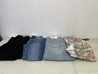Four pairs of women's pants folded and laid side by side: black, blue denim, light blue denim, and floral pattern.