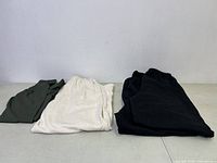 Four pairs of pants laid flat: two black joggers, one cream/off-white wide leg pant, one green leggings.