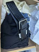 Photo of a black Zara belt with crocodile texture and a silver rectangular buckle lying on black and cream knit clothing in a box.