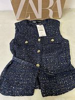 Navy blue tweed Zara vest lying flat with visible gold buttons, two front flap pockets, Zara tag attached, and original Zara box behind