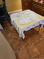 Overview of the vintage embroidered table linens collection laid out on a yellow tablecloth with crochet grape border in a kitchen setting.