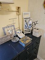 Full view of black metal jewelry trees, jewelry tower with mirror, tissue box cover, inspirational plaque, mini mirror wall piece, and decorative storage boxes on dark tabletop under wall-mounted light.