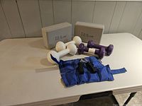 Entire set of exercise equipment on table, showing dumbbells, yoga blocks, ankle weight, and hand gripper