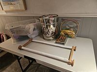 Overview of table with yarn, knitting needles, embroidery hoops, roll frame, and a metal Saks container