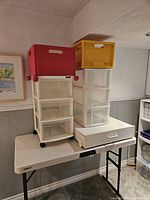 Photo showing two plastic drawer units with transparent drawers and colored boxes on top. Red box with wheels on left unit and yellow box on right unit.