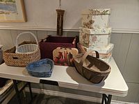 Overview of 10 assorted storage containers including baskets, fabric box, floral nesting boxes, and a decorative suitcase on a white folding table.