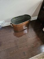 Side angle view of the antique copper laundry tub on wood floor showing full body and handles.