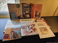 Photo showing all nine home improvement books arranged on a table near a window, displaying covers with various home decor themes and DIY project instructions.