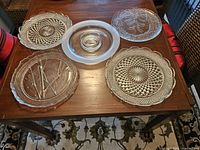 Overview of five glass serving pieces with various pressed and raised designs on a wooden table.