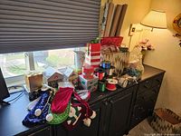 Gift wrapping supplies arranged on a dresser showing ribbons, decorative boxes, gift bags, and holiday-themed velvet and felt bags.