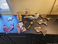 Wide view of the 8 art pieces including metal fish, animal figurines, and small decorative items on black surface near window