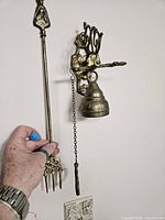 Side view of brass Celtic fire fork held by hand showing three prongs and decorative handle