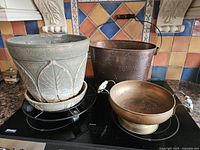 Full view of all four pieces: stone planter on saucer on black wheeled stand, copper bucket planter with butterflies, and copper pedestal bowl.