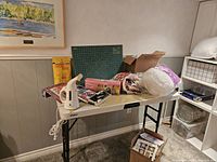 Wide view of quilting supplies set up on a folding table including cutting mat, rotary cutter, some fabric, and books.