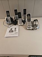 Four VTech cordless phones each on their white charging stand with power cords and a user manual included, showing overall set contents.