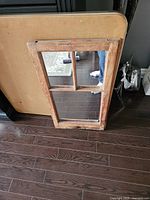 Full view of rectangular mirror made from reclaimed antique farmhouse window frame with divided glass sections, leaning against a table.