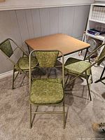 Full view of square card table with 3 folding chairs positioned around it, showing table top and chair upholstery pattern