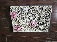 Close-up photo of textured 3D floral wall art showing detailed raised paisley and flower patterns in beige and mauve.