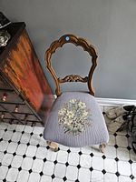Front view of Victorian solid wood chair showing carved backrest and hand embroidered floral seat upholstery.