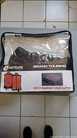 Front view of sealed packaging containing the vest liner showing brand Venture Heat Grand Touring Collection with images of heated vest on front and labeling 12V Heated Vest Liner.