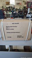 Boxed bike trainer front with label showing model number KW-7073-0220, quantity 1, made in China, Daymak certified product.