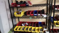 Metal shelving unit with a variety of plastic bins in red, yellow and blue filled with nuts, bolts, washers, electrical parts and small wheels.