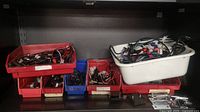 Shelf with various plastic storage bins filled with wires, connectors, and other electronic components. Hinges and metal plates placed on the shelf surface.
