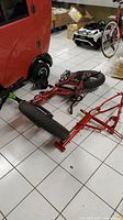Red disassembled electric bicycle frame and front tire on white tile floor