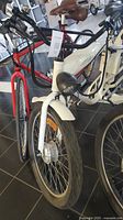 Front angled view of white Daymak electric bike showing front wheel, headlight, and frame.