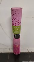Rolled pink Gaiam yoga mat with dot and floral pattern, showing front label with brand and product details.