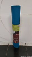 Front view of rolled blue Gaiam yoga mat with label showing brand and product type Yoga Mat, 6P Free, Super Grip Texture.