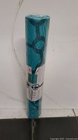 Rolled blue Jogi yoga mat with geometric pattern, plastic wrapped, showing front side with partial label visible.
