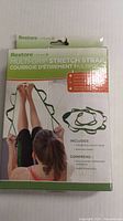 Front of the Restore Multi-Grip Stretch Strap box showing product image, branding, and usage example of a person stretching their legs using the strap.