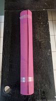 Rolled pink yoga mat secured with two clear straps on a black wooden surface.