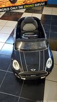 Front view of black Mini Cooper ride-on toy car showing realistic headlights, windshield, and padded seat.