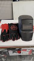 Pair of Lincoln Electric traditional MIG stick welding gloves black and red with flame design, and Prostar welding mask in black with adjustable headgear and flip-up lens cover.