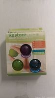 Front view of the green, purple, and blue therapy balls in packaging labeled 'Restore Hand Therapy Kit' with exercise guide indication.