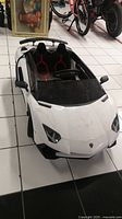 Front and side view of white Lamborghini Aventador ride-on toy car showing detailed headlight decals, windshield, and seating area.