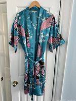 Front view of a light blue silk Japanese robe with pink peacocks and white flowers, hung on a wooden hanger.