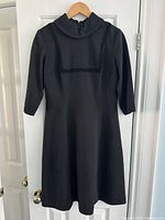 Full front view of the handmade black 1960s dress on hanger showing overall design and silhouette.