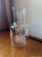 Full view of clear glass carafe with pink rose floral patterns around the body, straight sides and flared rim.