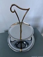 Front view close-up of the top tray and brass-tone atomic starburst style handle of the two-tiered dessert tray.