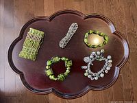 Photo of five different green bracelets arranged on a wooden flower-shaped table